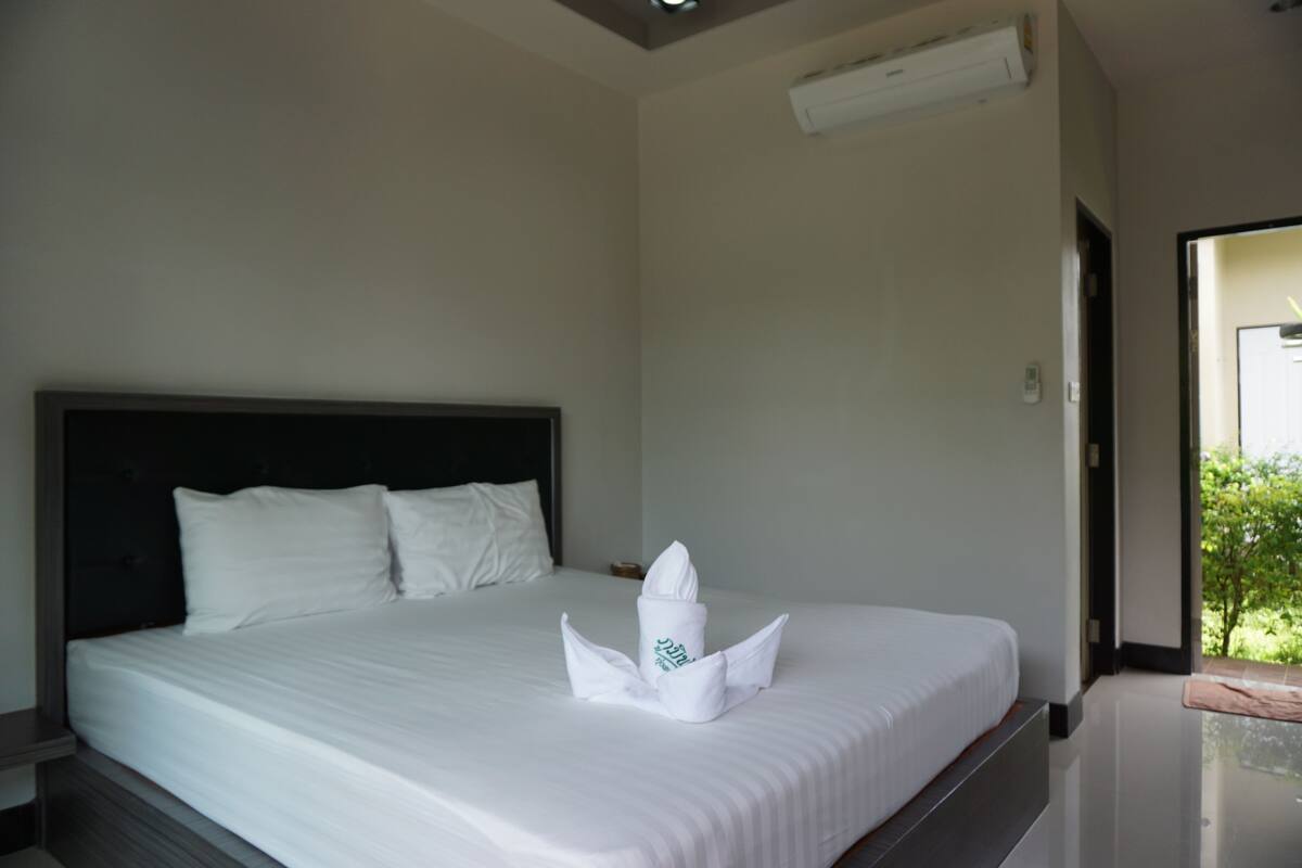A hotel room with a neatly made bed, a headboard, and a window with a view of greenery.