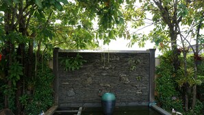 Un jardín con fuente, muro de piedra y plantas en macetas.