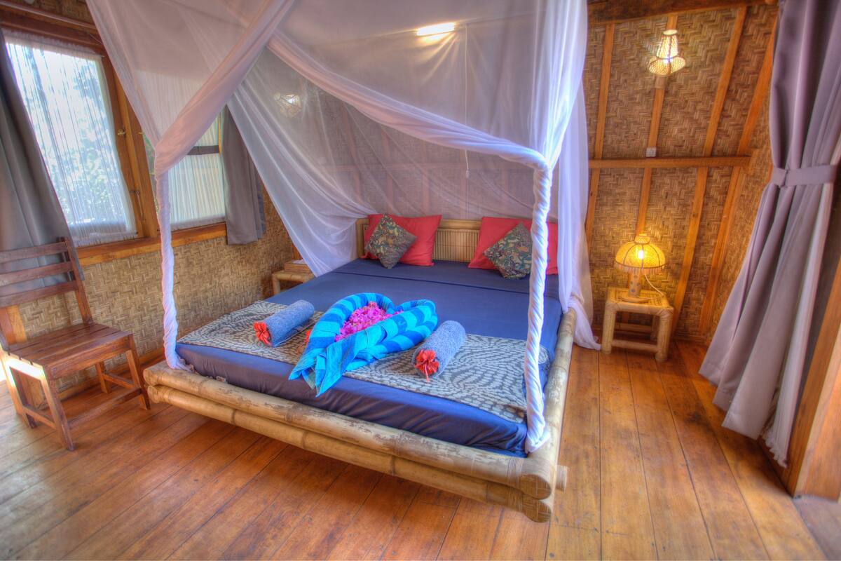 A bed with a canopy, wooden floor, and a nightstand with a lamp.