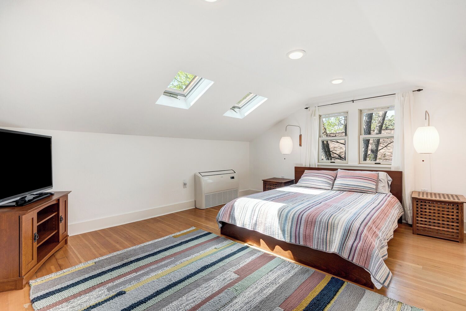Ein Schlafzimmer mit einem großen Bett, einem Fernseher, einer Heizung und Dachfenstern.