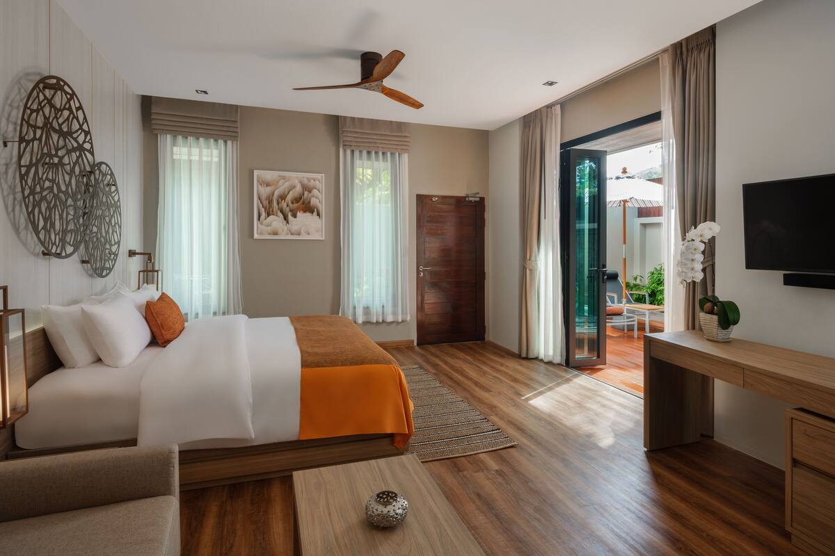 A modern hotel room with a large bed, a desk, a ceiling fan, and a TV.