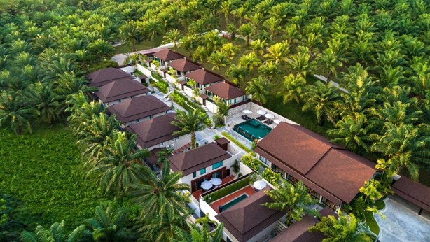 Un resort con varias construcciones tipo cabaña, un área de piscina central y exuberante vegetación tropical que rodea la propiedad.
