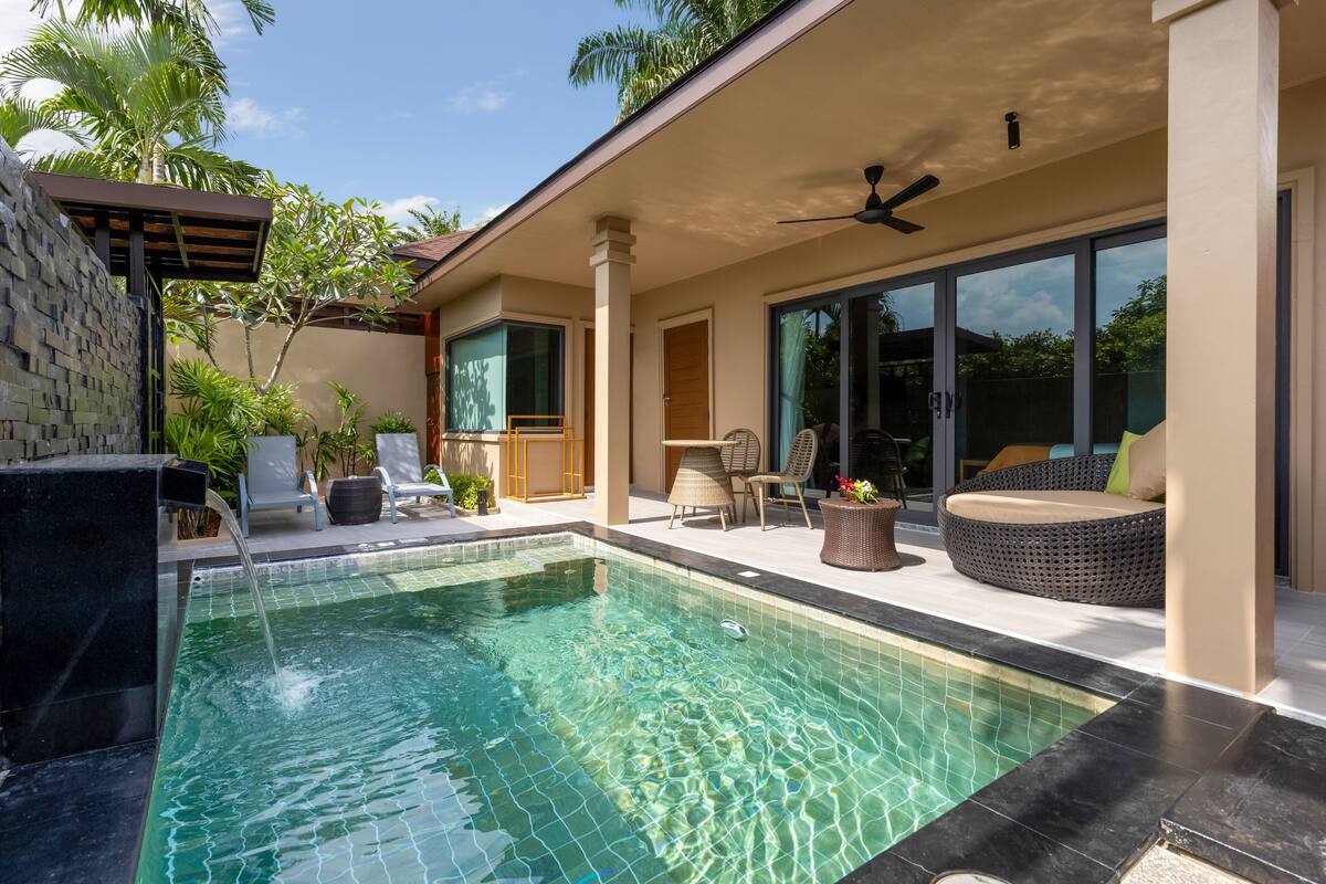 A swimming pool with a stone wall, lounge chairs, and a covered seating area.