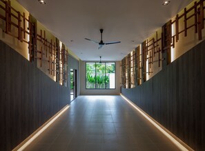 A modern hallway with a ceiling fan, wooden wall panels, and a large window at the end.