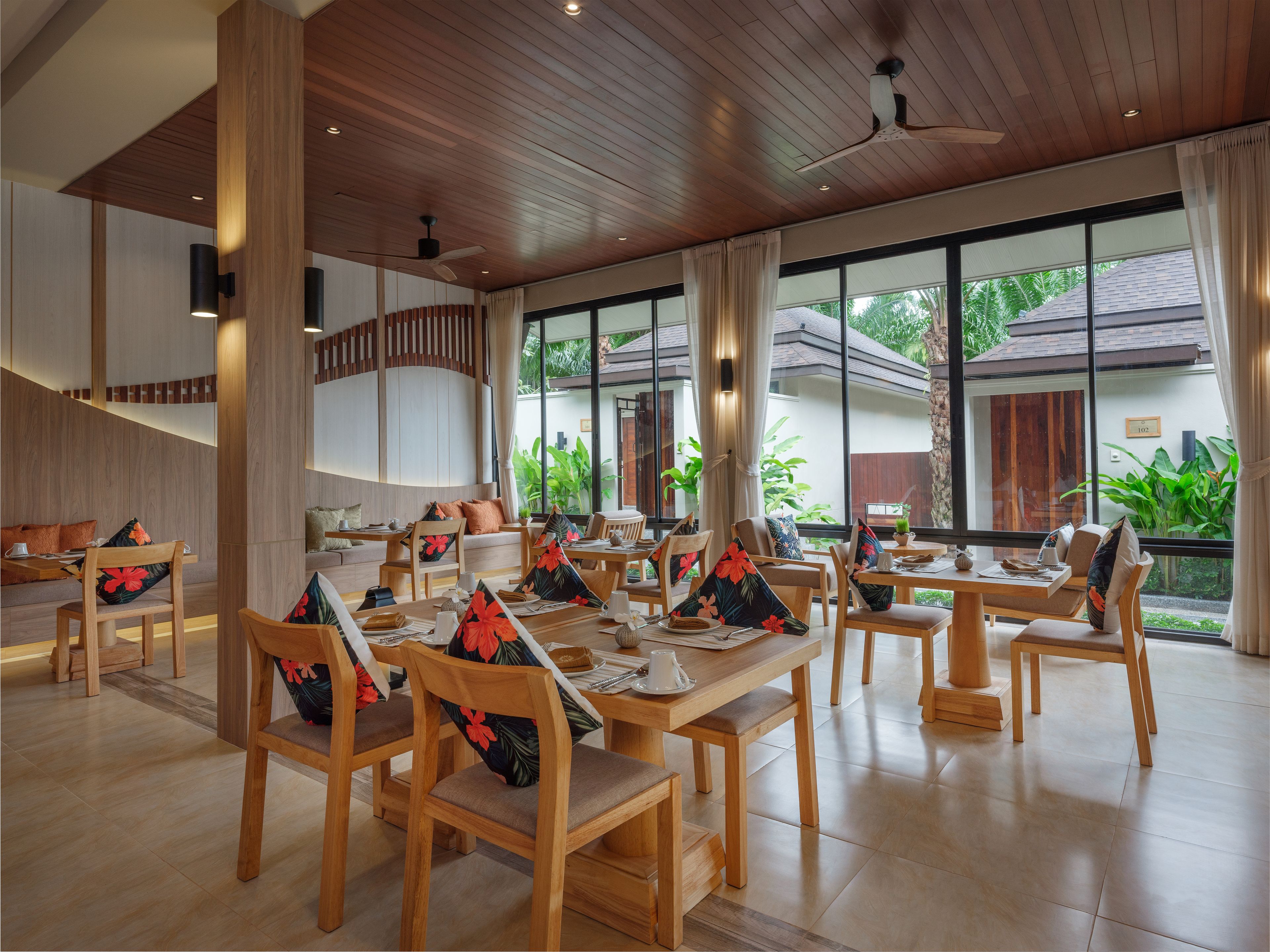 A spacious dining area with wooden furniture, large windows, and a view of greenery outside.