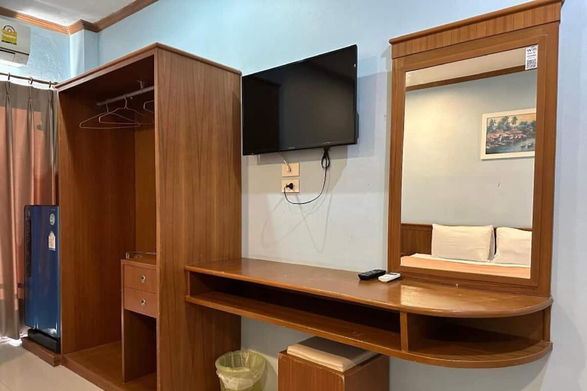 A bedroom with a wooden wardrobe, a flat-screen TV mounted on the wall, a bedside table, and a mirror.