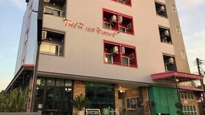 A multi-story building with balconies, large windows, and a sign with Thai text.
