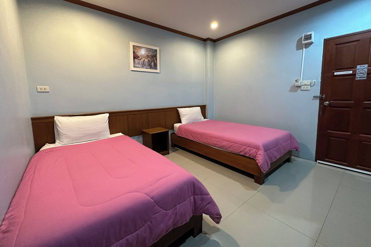 A hotel room with two beds, a wooden headboard, a small bedside table, a wall-mounted air conditioner, and a door with a no-smoking sign.