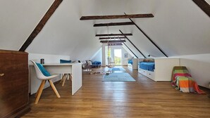 Amplia habitación en ático con techo inclinado, vigas de madera, un escritorio con silla, una cama y una manta colorida.