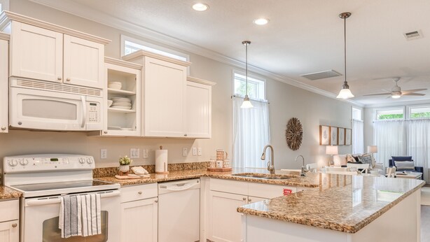 A modern kitchen with white cabinetry, a granite countertop, a built-in oven, and a large island with a sink.