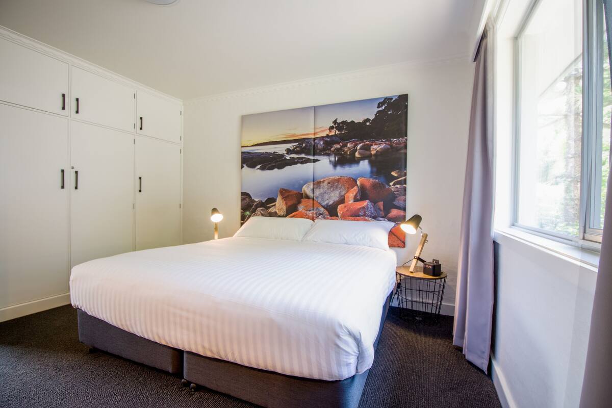 Une chambre avec un grand lit, une armoire blanche et un tableau représentant un paysage accroché au mur.