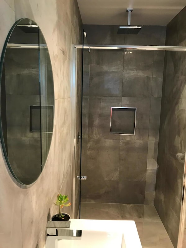 A modern bathroom with a glass-enclosed shower, a round mirror, and a small potted plant.