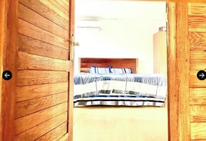 A wooden door leading to a bedroom with a bed, a headboard, and a wardrobe.