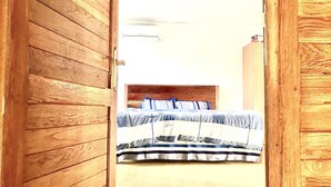 Una stanza con una porta in legno, un letto con copriletto a righe e una parete bianca.
