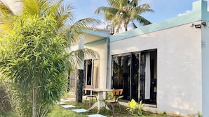 Una casa moderna con un patio dotato di tavolo e sedie, immersa nel verde e palme.