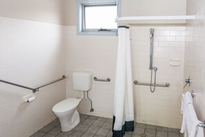 A bathroom with a toilet, grab bars, a shower, and a window. - Merimbula Lakeview Hotel (Merimbula)
