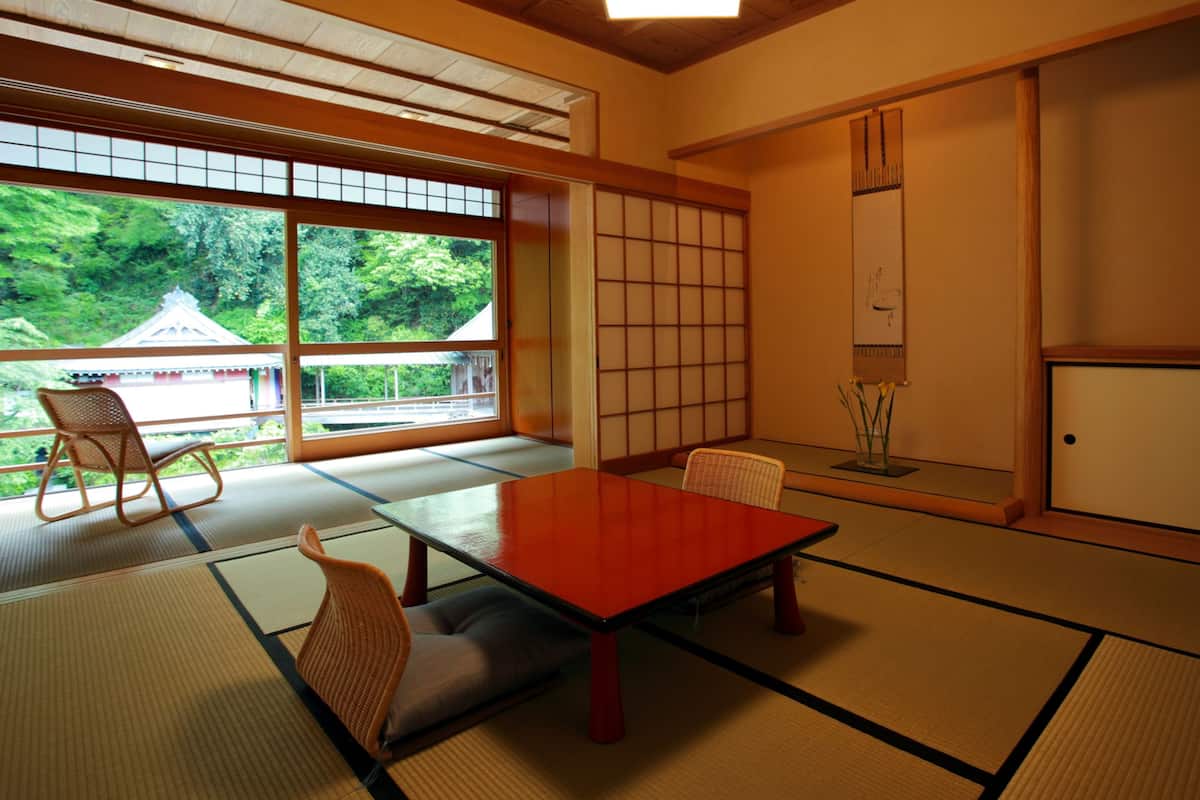 A traditional Japanese room with tatami flooring, a low table, and a view of a temple through large windows.