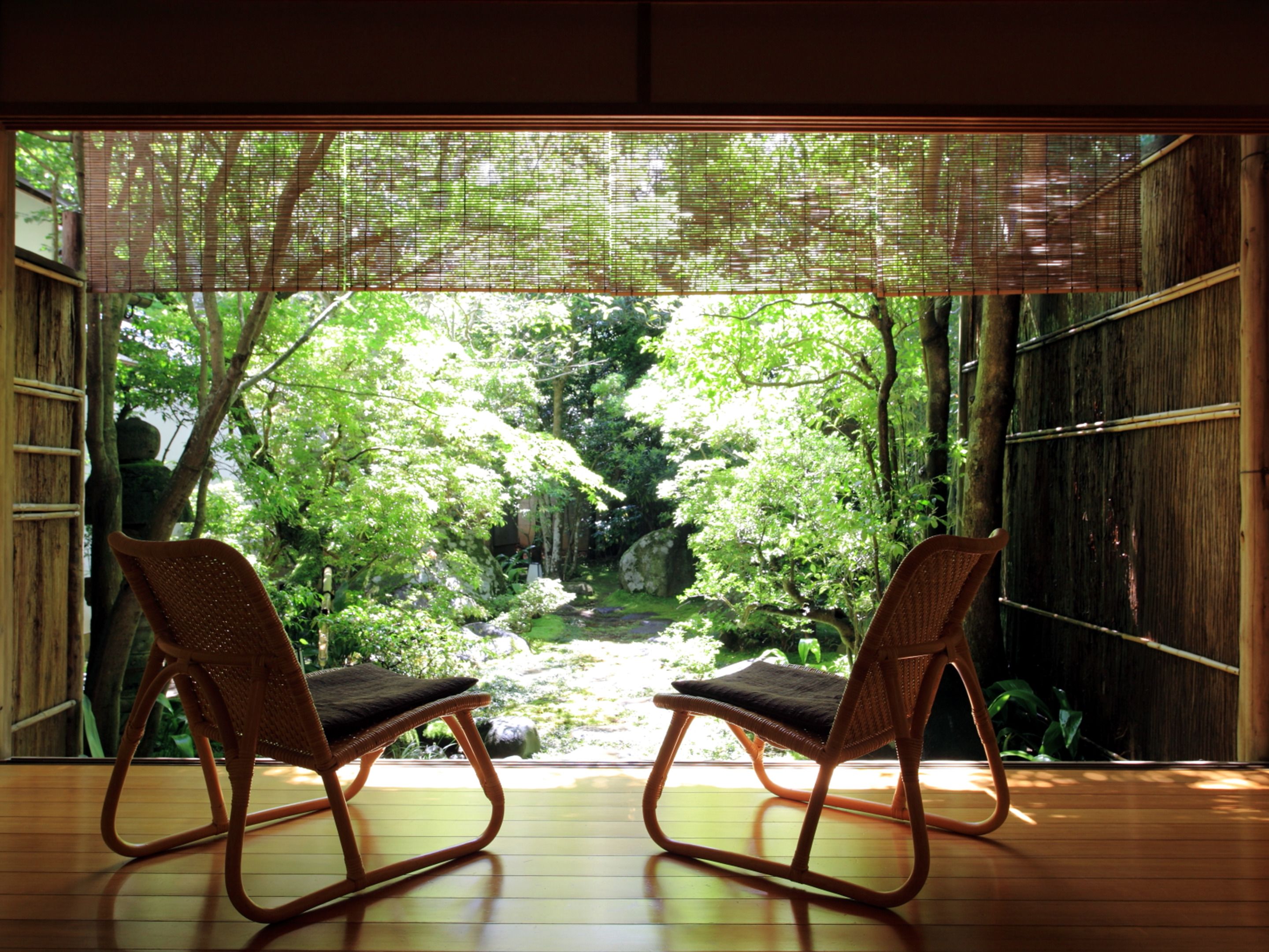 Ein Zimmer mit zwei Korbstühlen, die auf einen üppigen Garten durch eine Bambusabtrennung blicken.