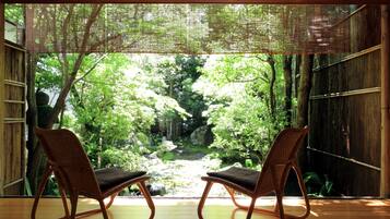 Ein Zimmer mit zwei Korbstühlen, die auf einen üppigen Garten durch eine Bambusabtrennung blicken.