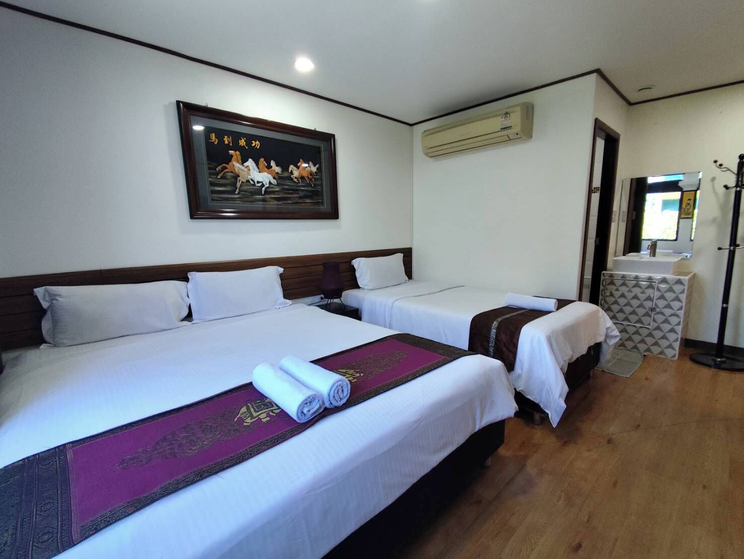 A hotel room with two beds, a framed picture on the wall, an air conditioning unit, and a small desk with a mirror.