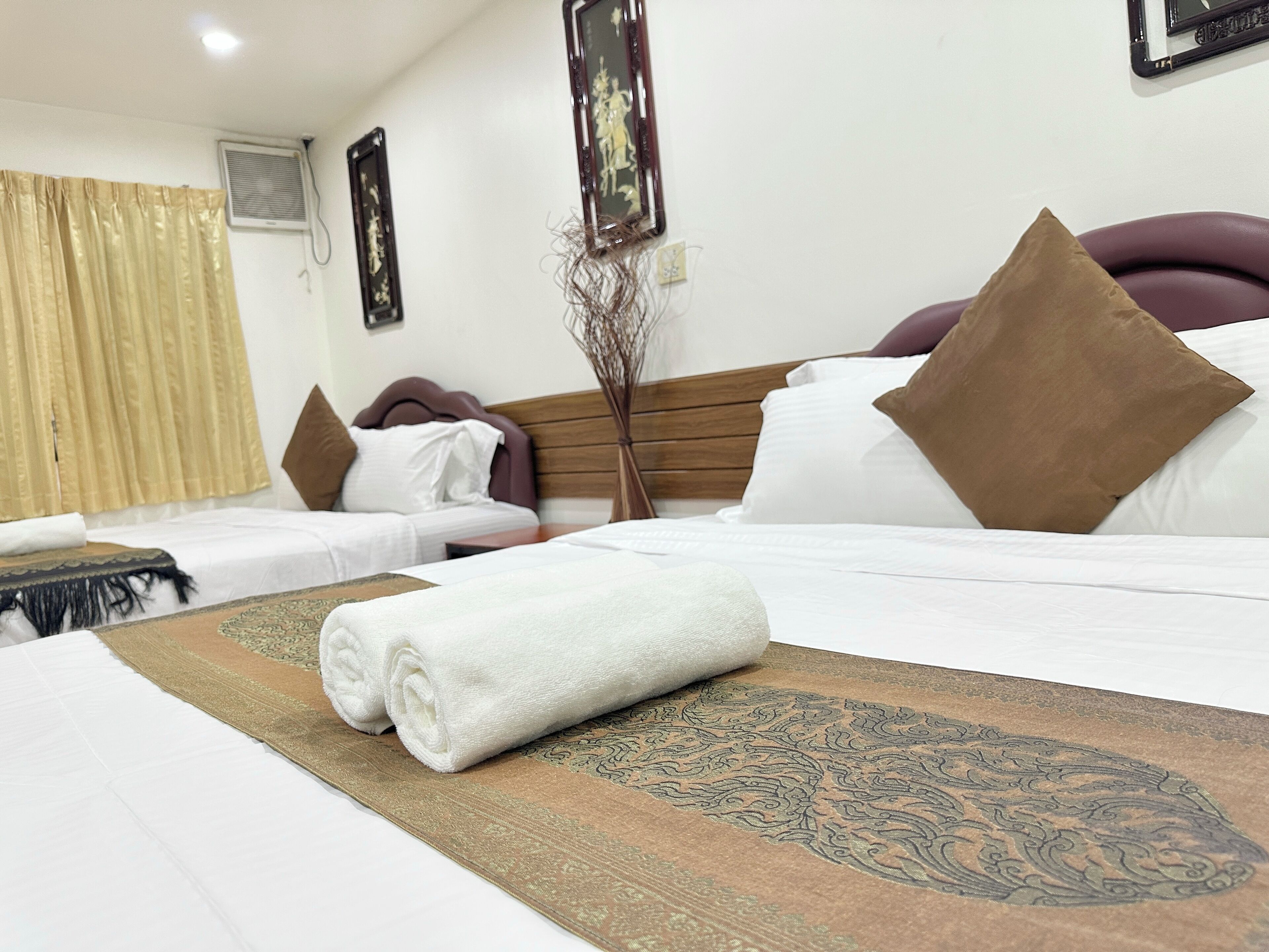 A hotel room with a neatly made bed, a decorative rug, and a wall-mounted air conditioner.