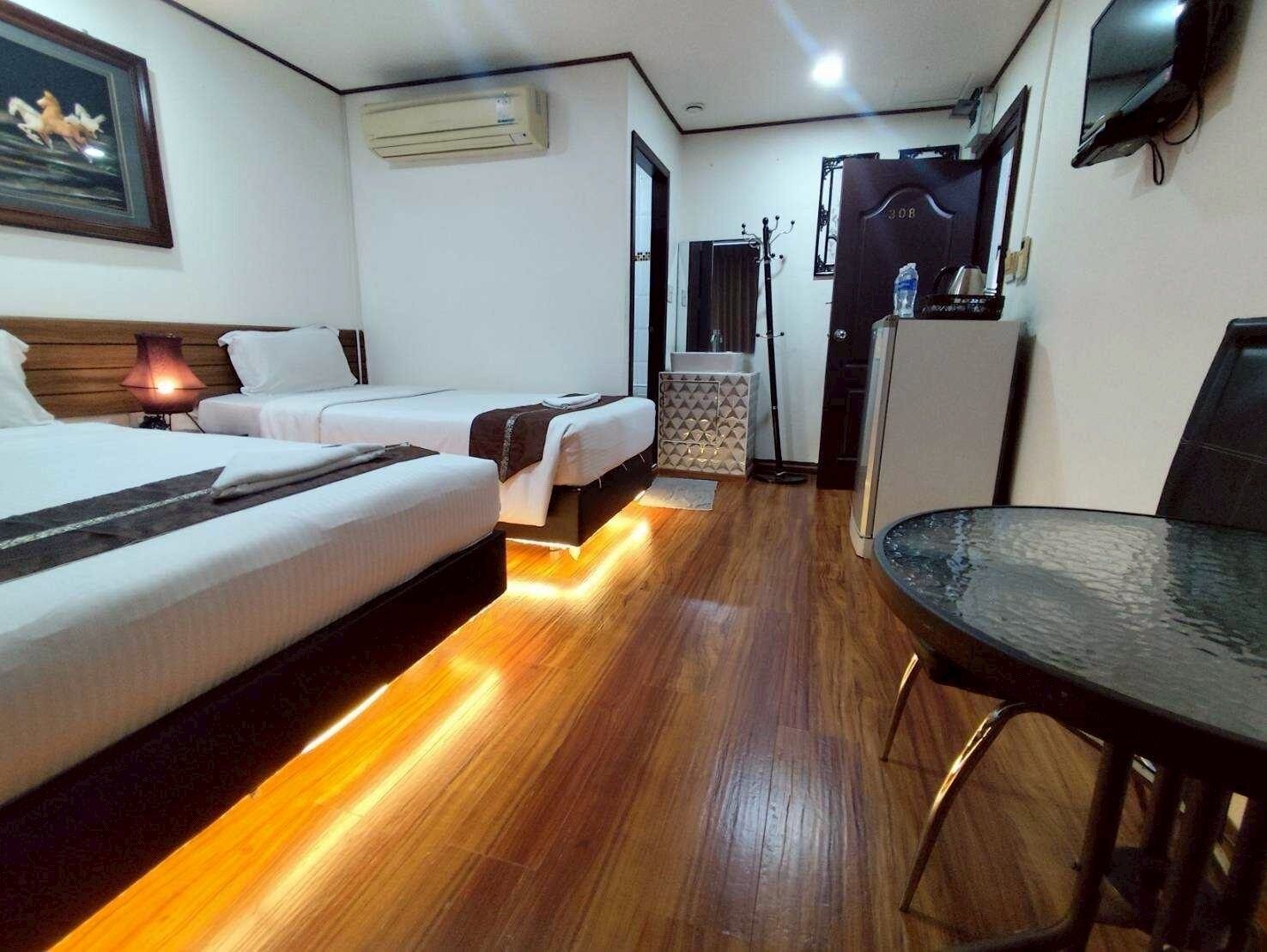 A hotel room with two beds, a desk, a chair, a TV, and an air conditioning unit.