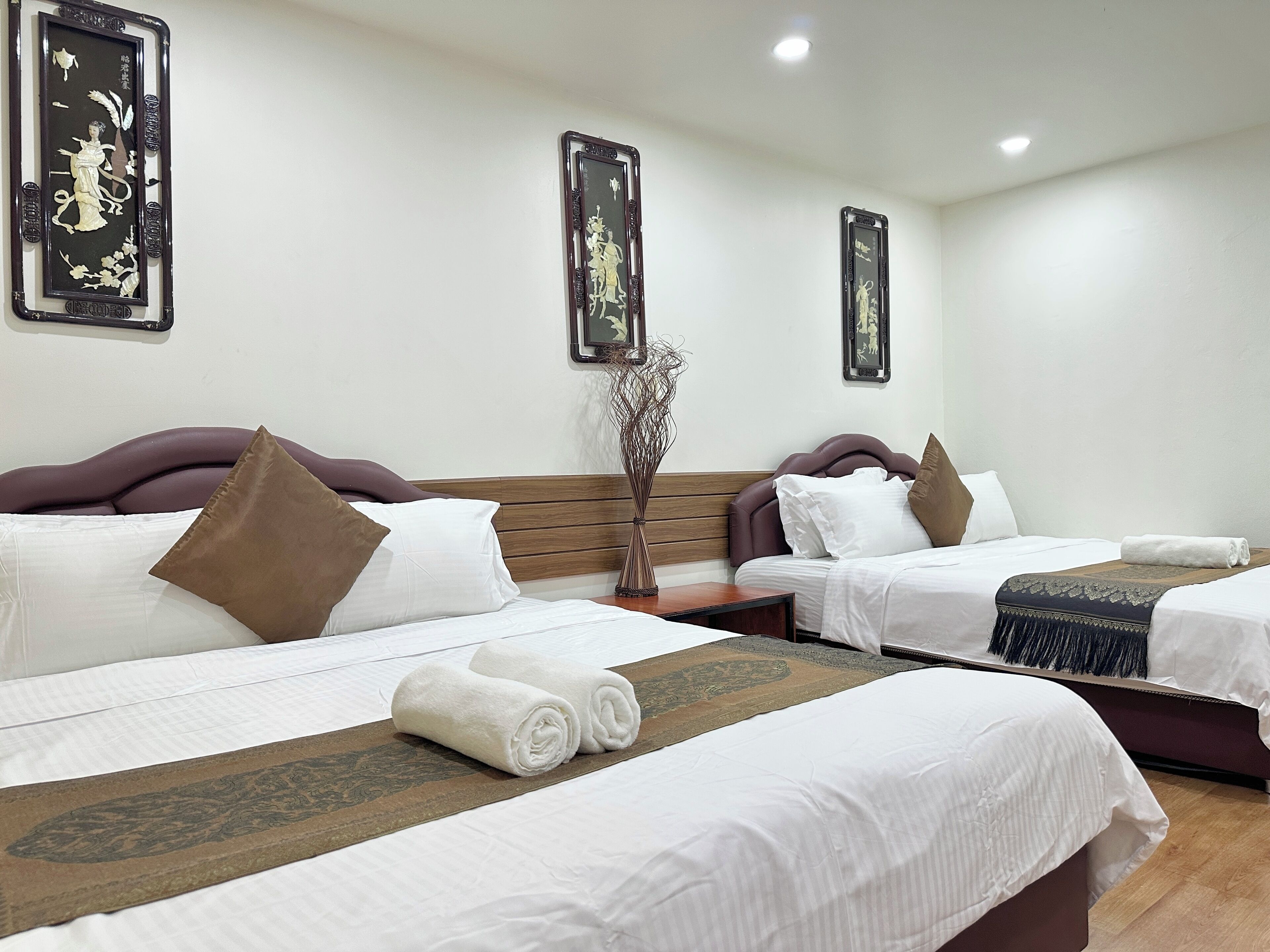 A hotel room with two beds, each with white linens and brown pillows, a wooden headboard, and a decorative wall hanging above each bed.