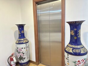 Elegant vases adorn the floor beside the elevator, complemented by a fire extinguisher for added safety.