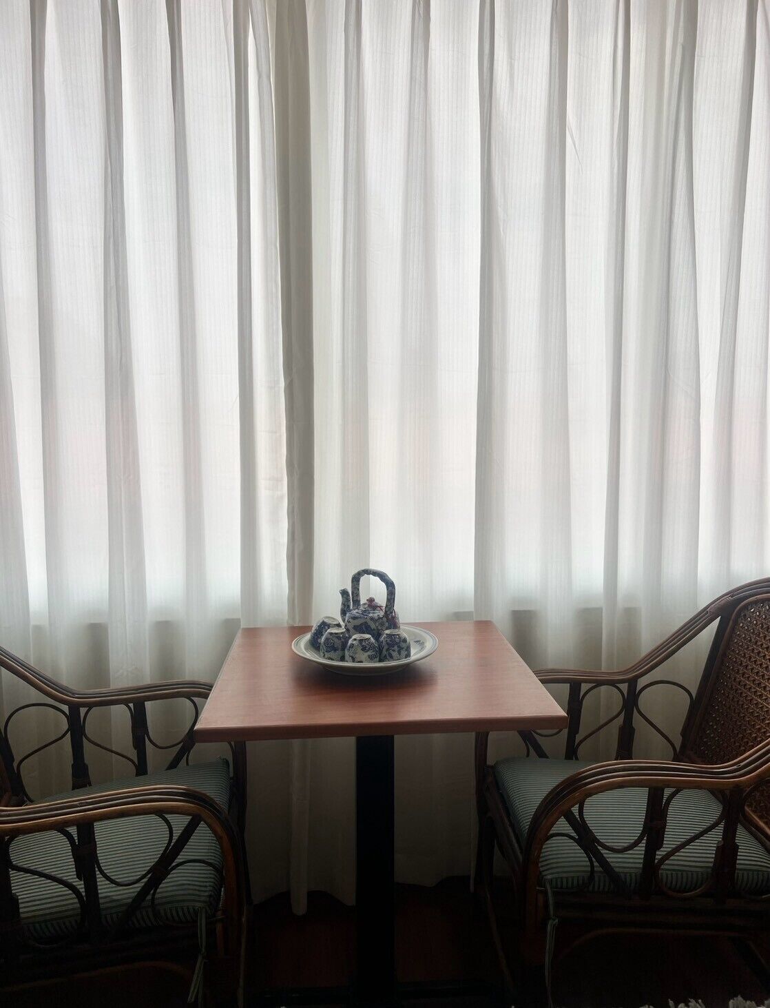 A room with a table and chairs, a tea set on the table, and sheer curtains in the background.