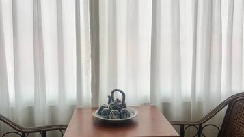 A room with a table and chairs, a tea set on the table, and sheer curtains in the background.