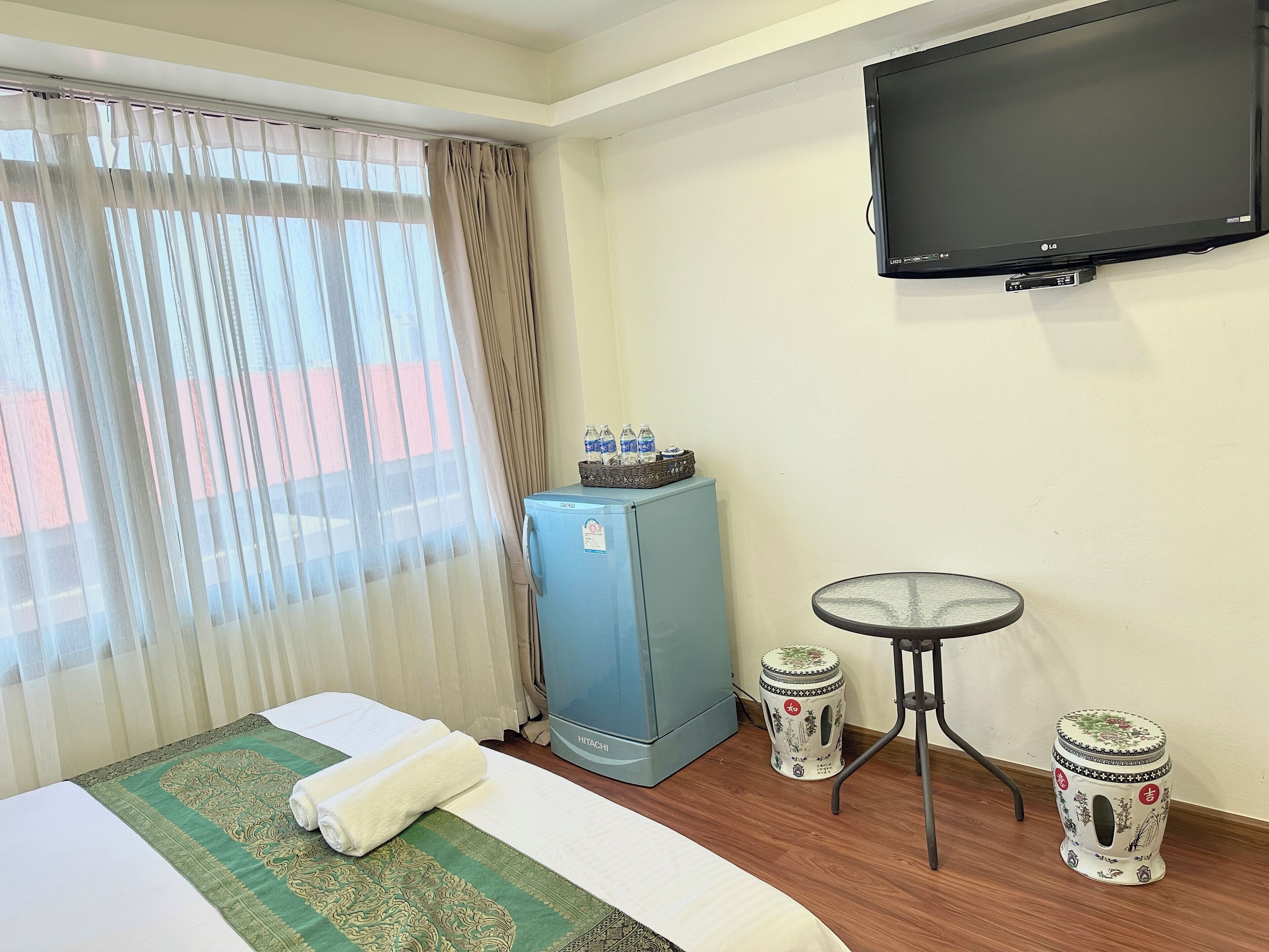 Une chambre d’hôtel équipée d’un lit, d’une télévision, d’un minibar, d’une petite table et de quelques tabourets décoratifs.