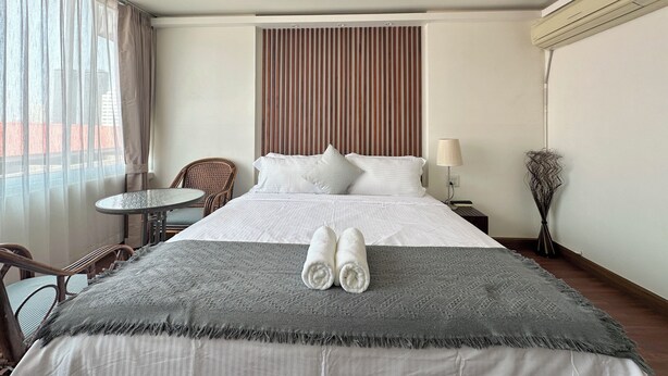 A hotel room with a bed, a chair, a small table, and a lamp. - Longzhu Guesthouse (Bangkok)
