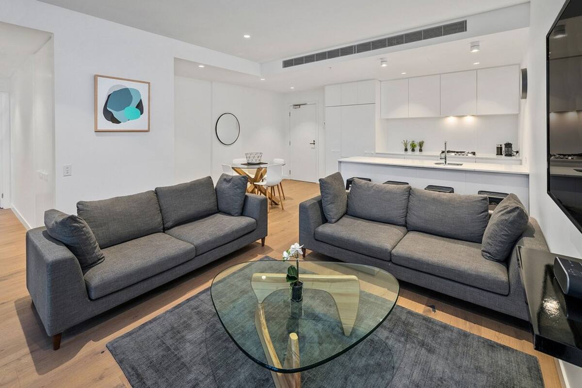 A modern living room with two grey sofas, a glass coffee table, and a small dining table with chairs.