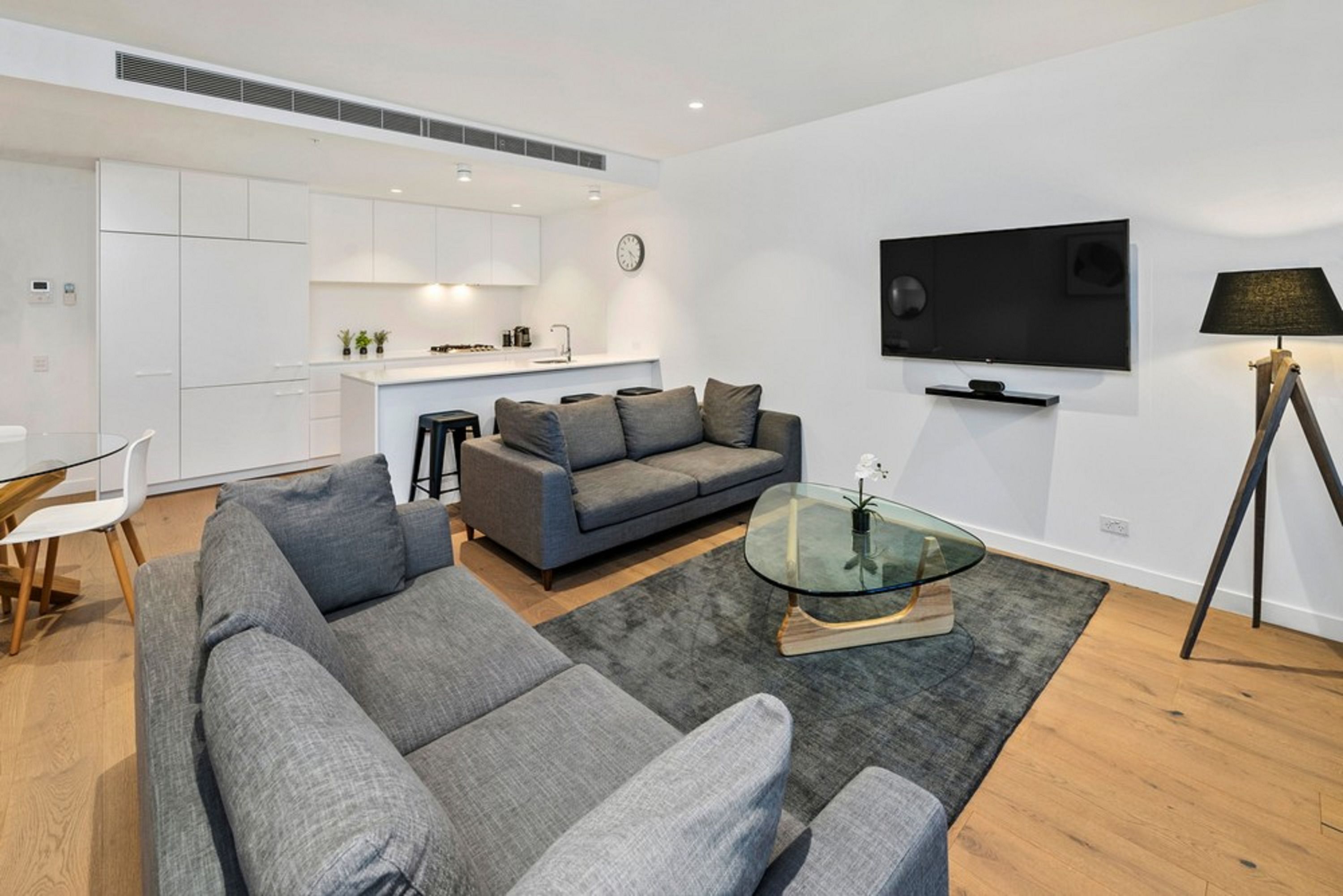 Un salon moderne avec un canapé gris, une table basse en verre et un téléviseur à écran plat fixé au mur.