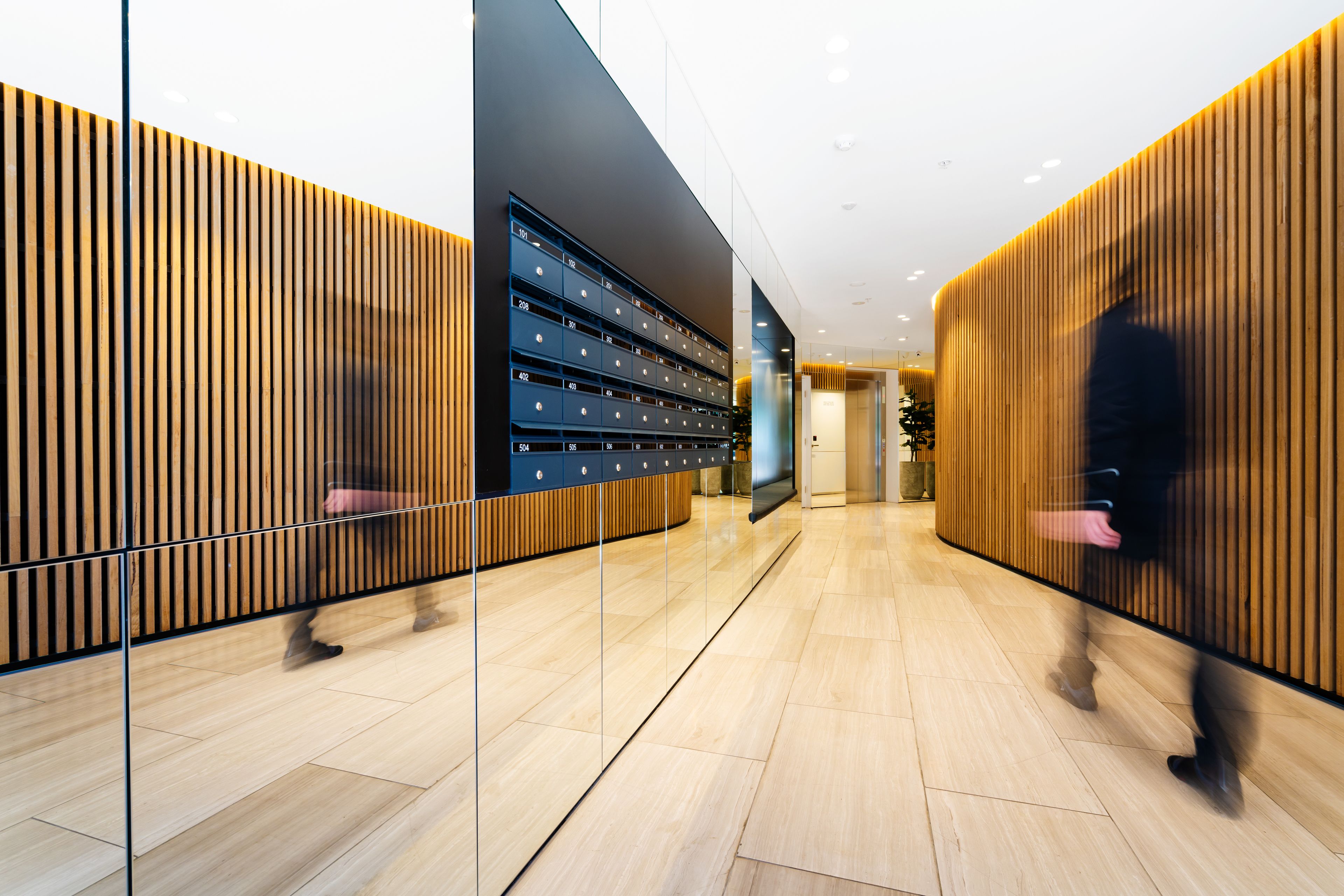 Un hall d’hôtel moderne avec un comptoir d’accueil en bois, une cloison en verre et une rangée de casiers.