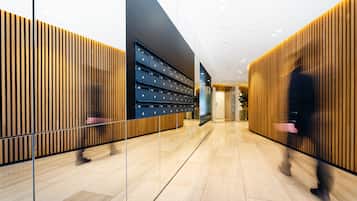 Un vestíbulo moderno de hotel con un mostrador de recepción de madera, un separador de vidrio y una fila de taquillas.