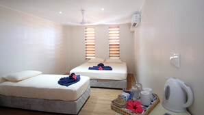 Habitación de hotel con dos camas, ventilador de techo, aire acondicionado, hervidor de agua y bandeja con artículos de aseo.