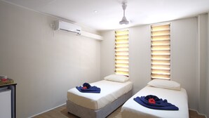 Una habitación con dos camas individuales, ventilador de techo, aire acondicionado y una pequeña mesa con una cesta.