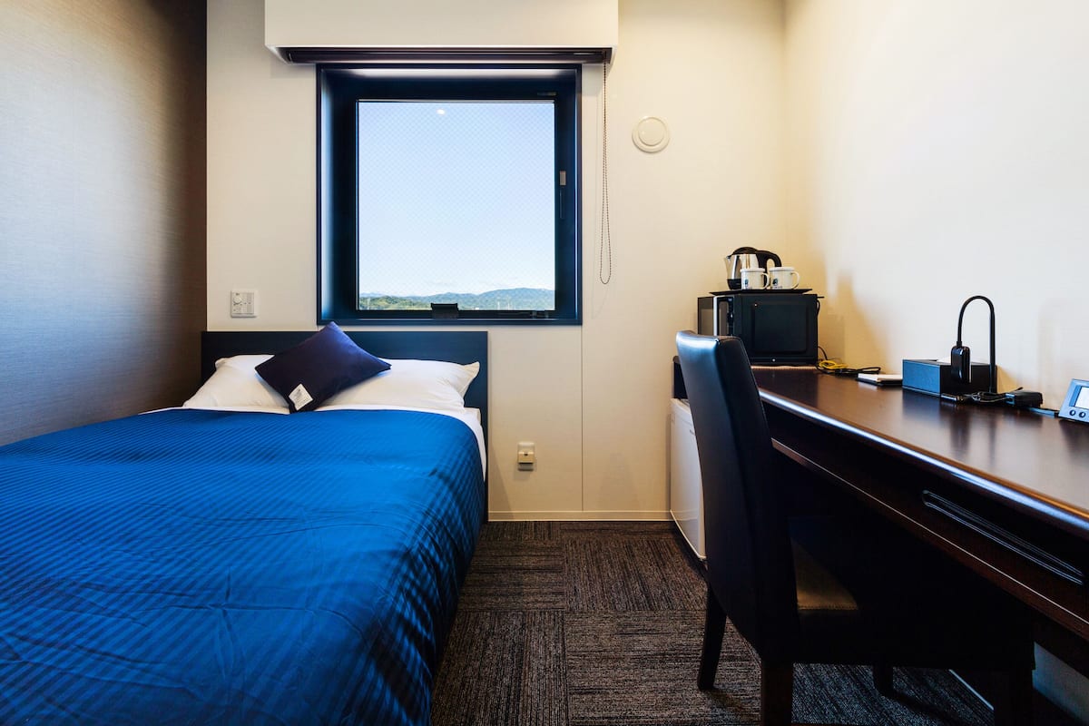 A hotel room with a bed, a desk, a chair, a window, and a view of the outdoors.