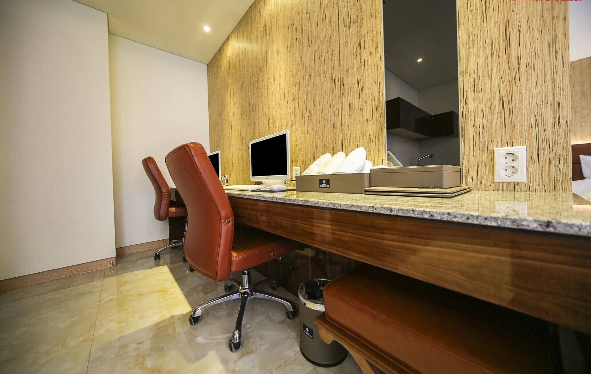 Une chambre d’hôtel avec un bureau en bois, une chaise de bureau rouge, un ordinateur et une boîte de mouchoirs.