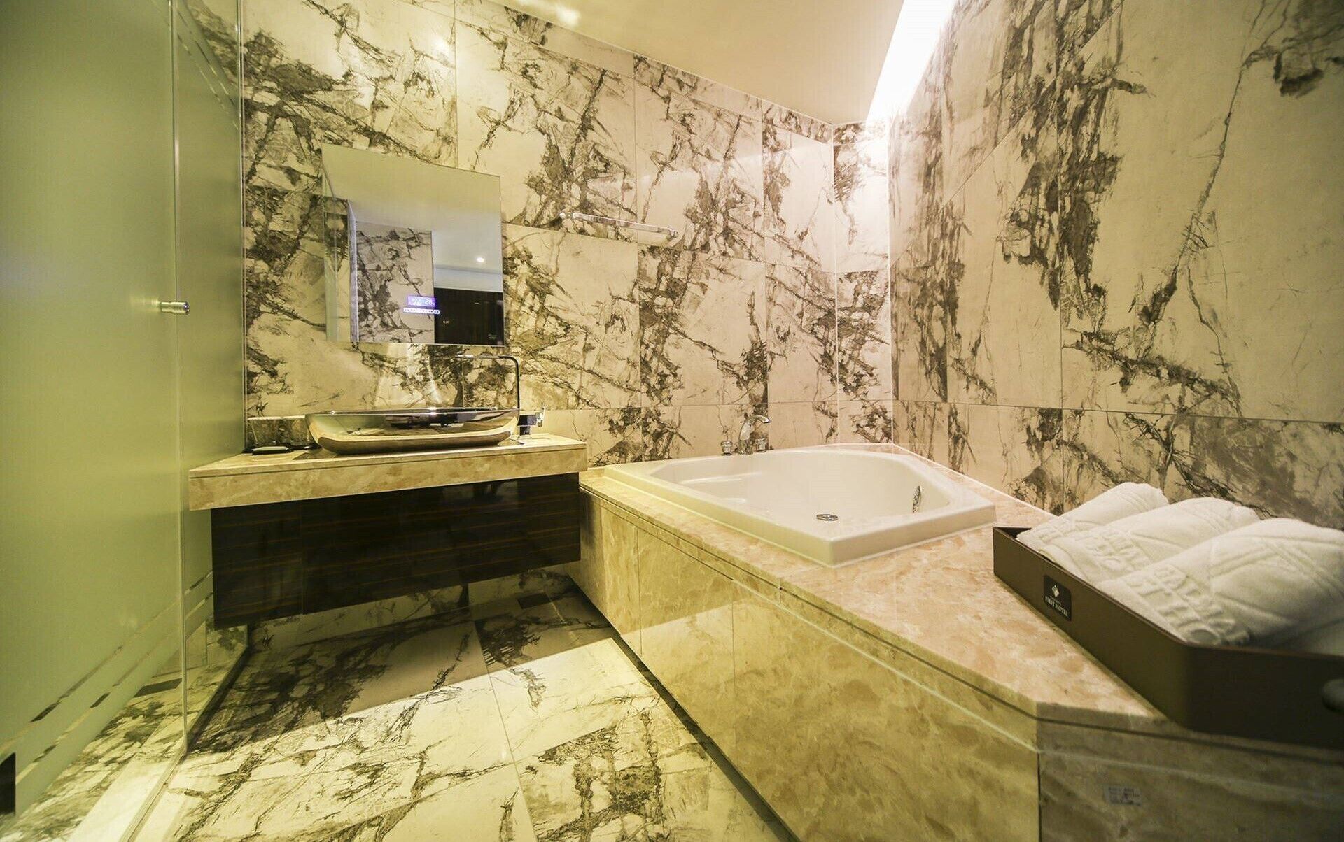 A bathroom with a marble wall, a bathtub, a vanity with a mirror, and a towel rack.