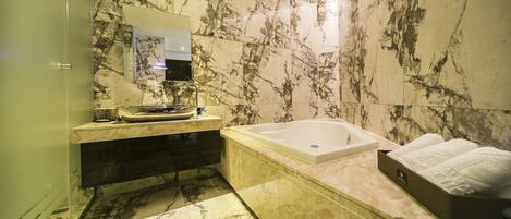 A bathroom with a marble wall, a bathtub, a vanity with a mirror, and a towel rack.