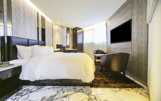 A modern hotel room with a large bed, a desk, a chair, and a TV.