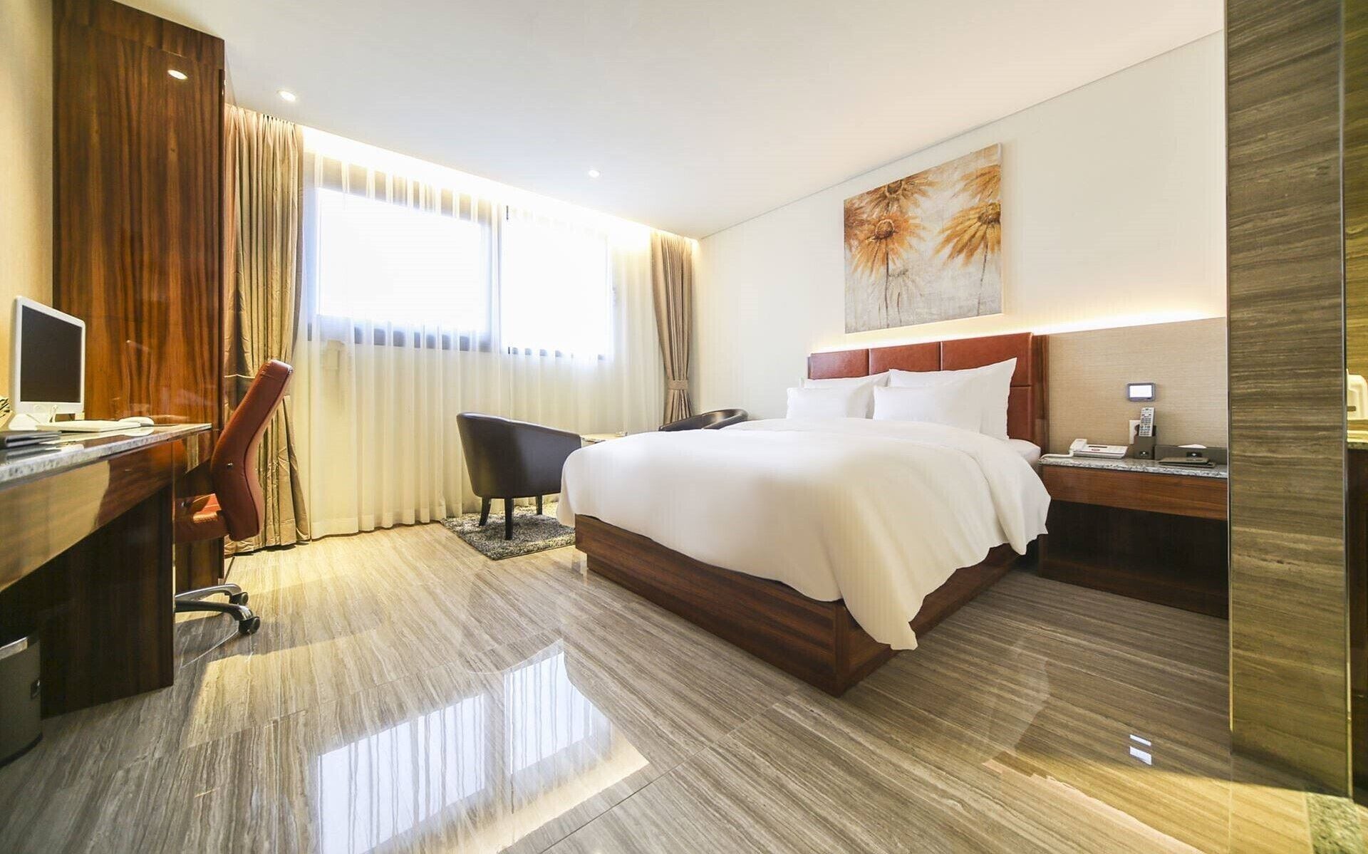Una habitación de hotel con cama, escritorio, silla y un cuadro en la pared.