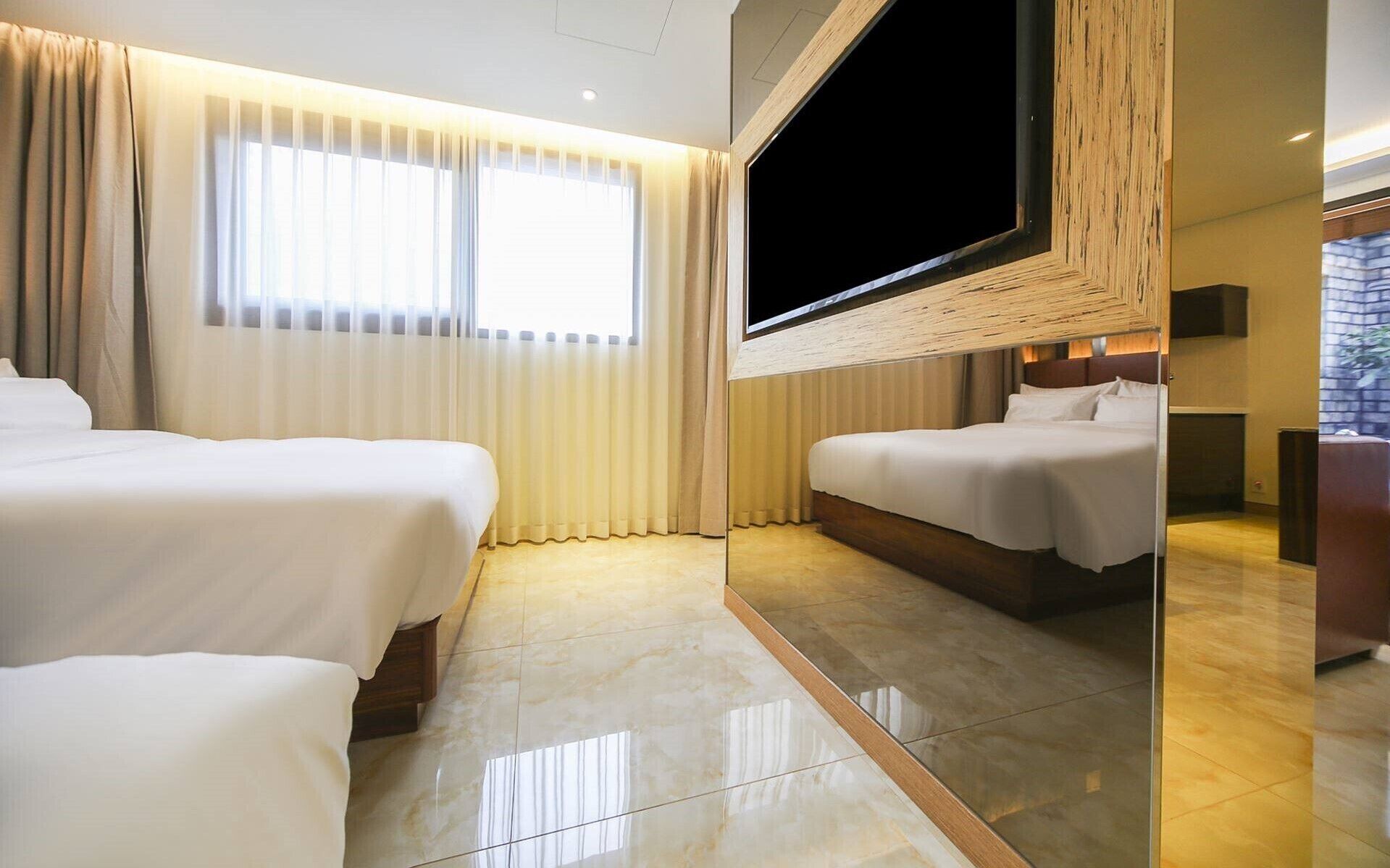 A hotel room with two beds, a large TV, and a view of the outdoors.