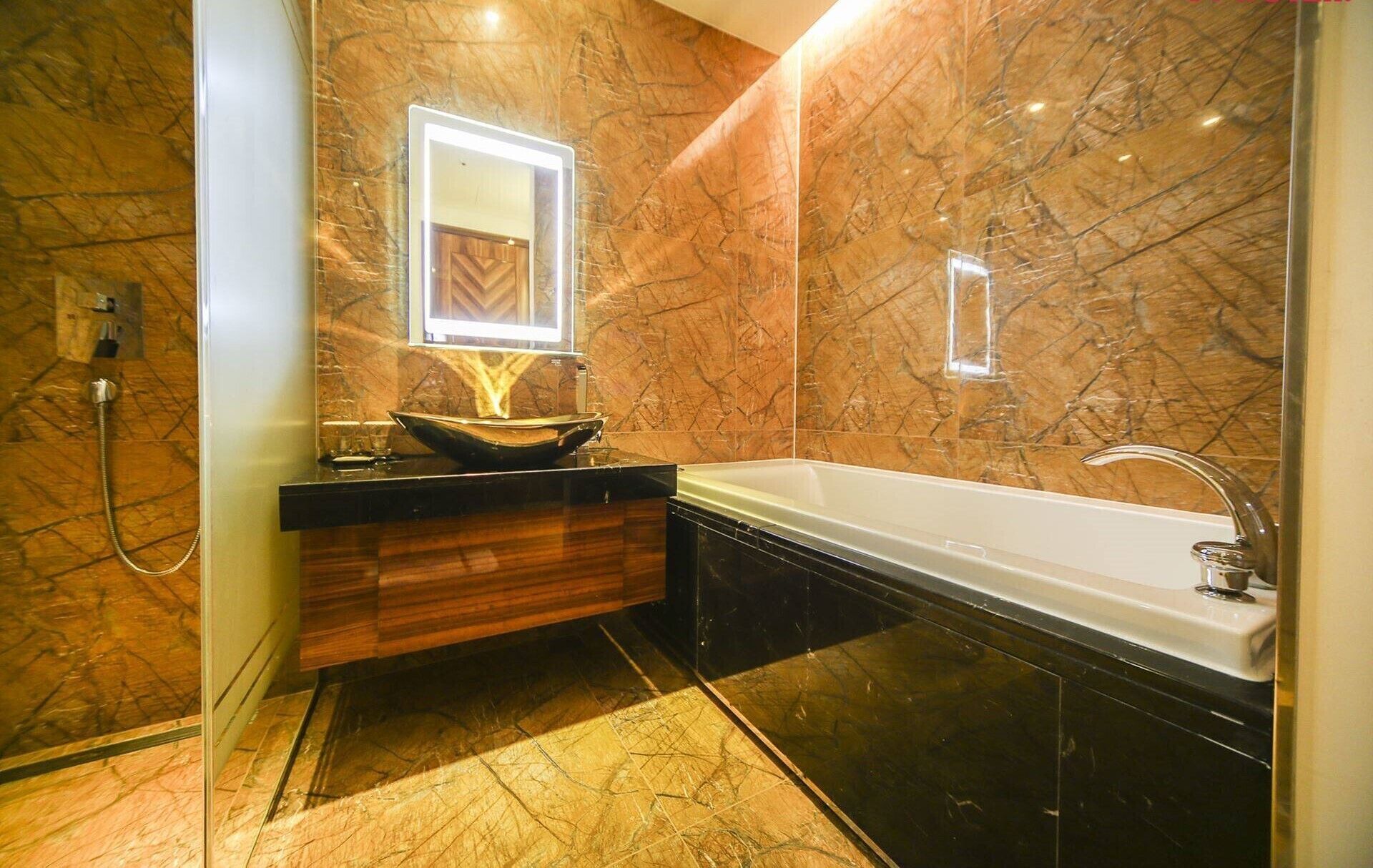 A modern bathroom with a marble floor, a wooden vanity, a large bathtub, and a mirror with a light.