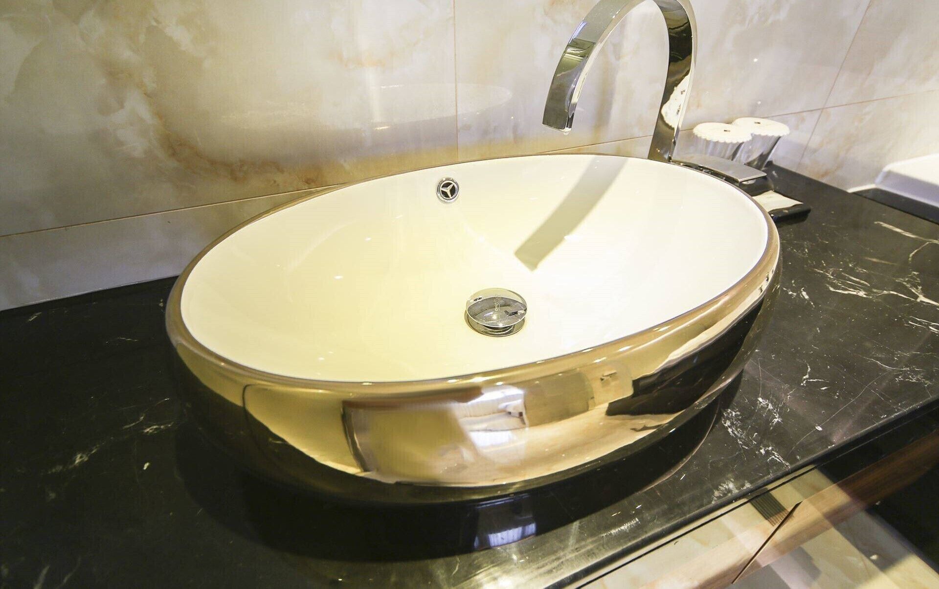 A round, white sink with a single faucet, set against a marble wall.