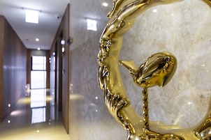 A hallway with a reflective golden sculpture, marble walls, and a modern ceiling design.