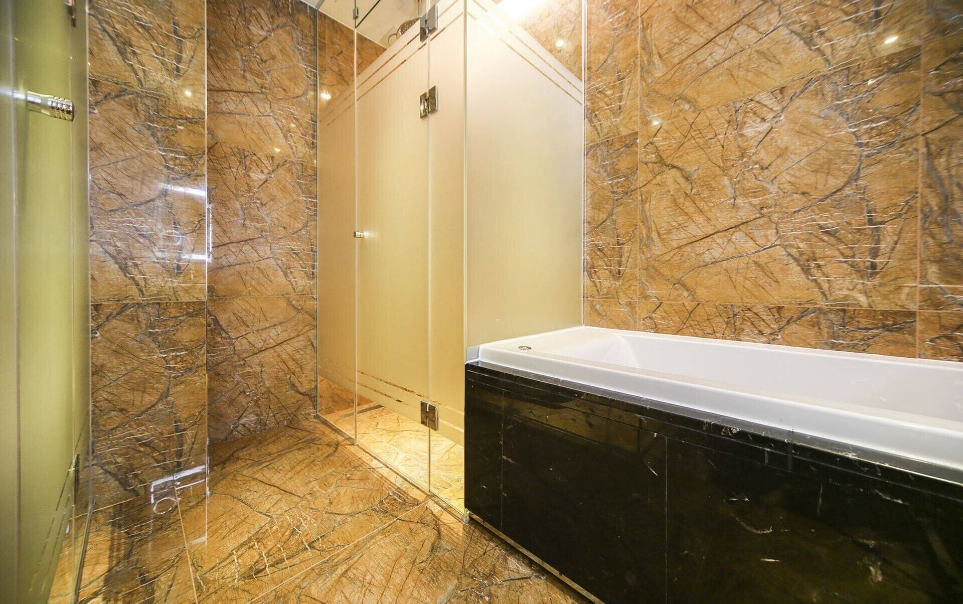 Un baño con pared de mármol, cabina de ducha de vidrio y bañera negra.