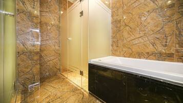 Un baño con pared de mármol, cabina de ducha de vidrio y bañera negra.